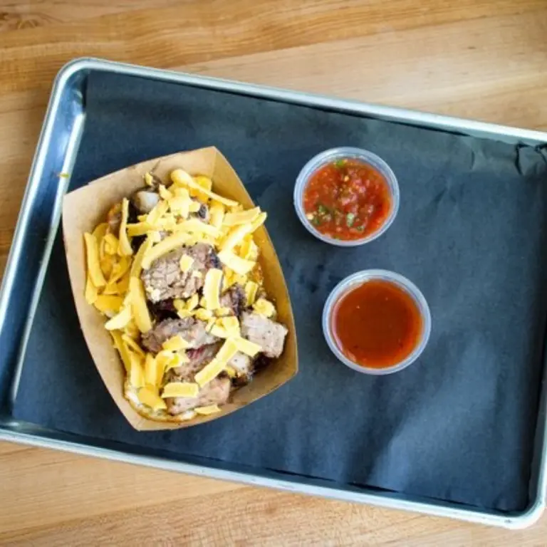 Plate with a breakfast bowl that has eggs, brisket, and cheese with salsa on the side.